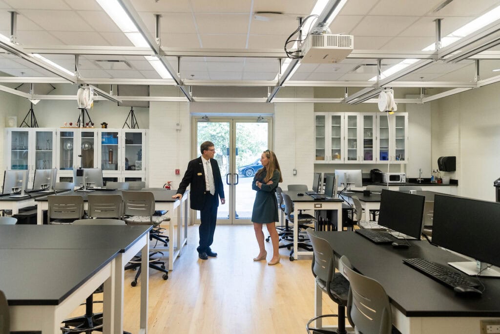 Two people standing in a classroom with desks and computers.