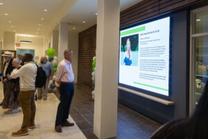A man stands in a foyer, watching a slideshow on a screen on the wall 