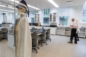 A skeleton in a lab coat and hat sits in a bright, open laboratory 