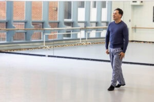A man stands in a dance studio, with a mirror behind him