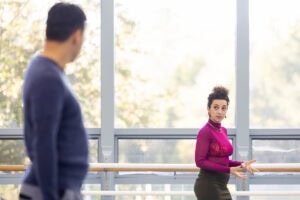 A woman in a magenta turtleneck looks over at a man in a blue shirt