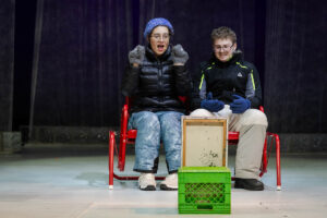 Two actors sit together onstage while reherasing a scene 