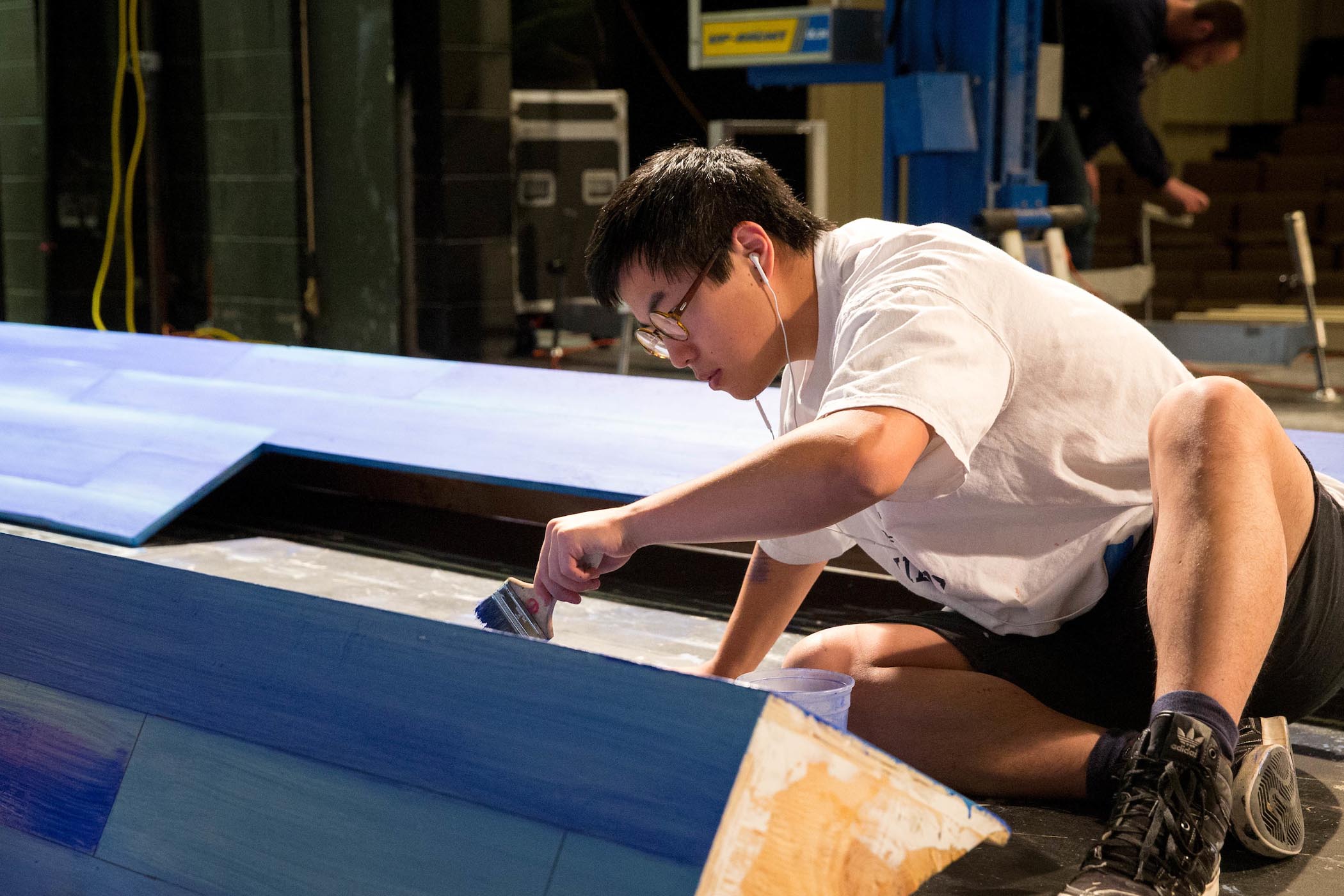 Male student paints stage scenery.